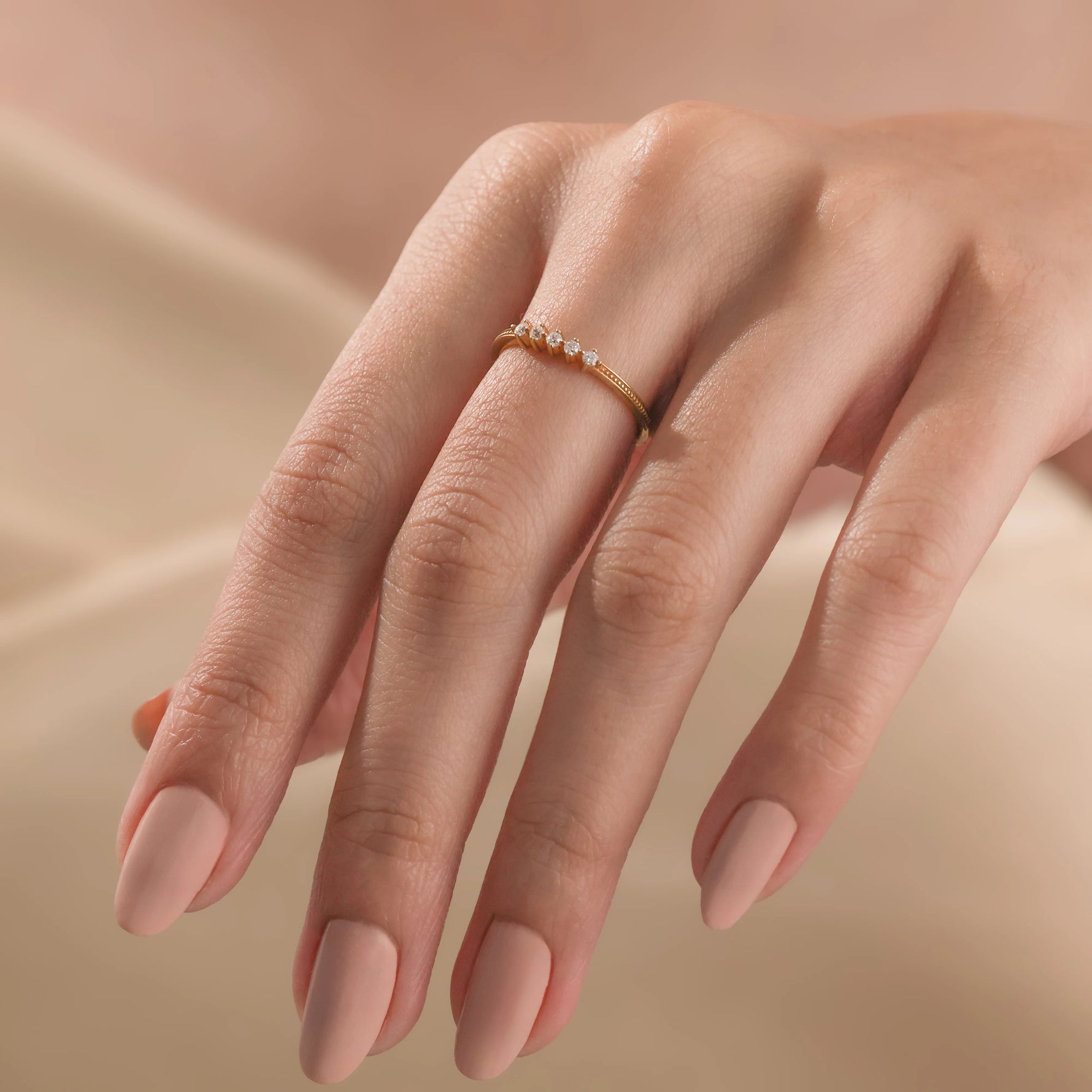 A woman wearing a dainty yellow gold stacking ring featuring a linear cluster of five small round diamonds.