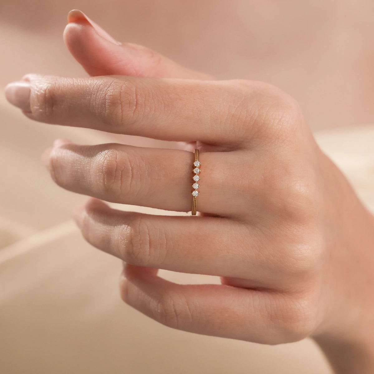 Dainty five-stone diamond ring in yellow gold with delicate beaded edge detailing, modeled on a woman's finger. Stackable minimalist band.