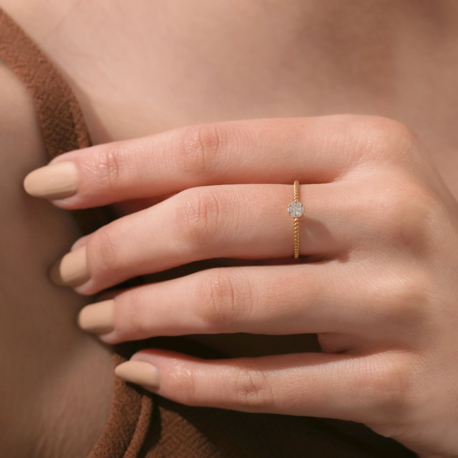 A minimalist yellow gold promise ring featuring a dainty round diamond cluster centerpiece and a twisted band design worn on a hand.