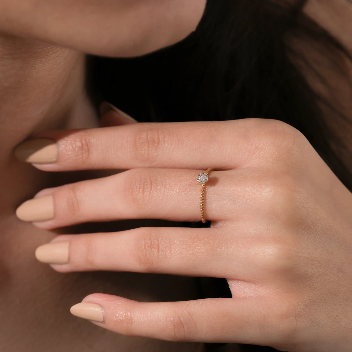 Close up of a delicate 14k yellow gold stackable ring with a small circular diamond cluster setting on a finger with nude manicure.