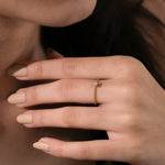 Close up of a delicate 14k yellow gold stackable ring with a small circular diamond cluster setting on a finger with nude manicure.