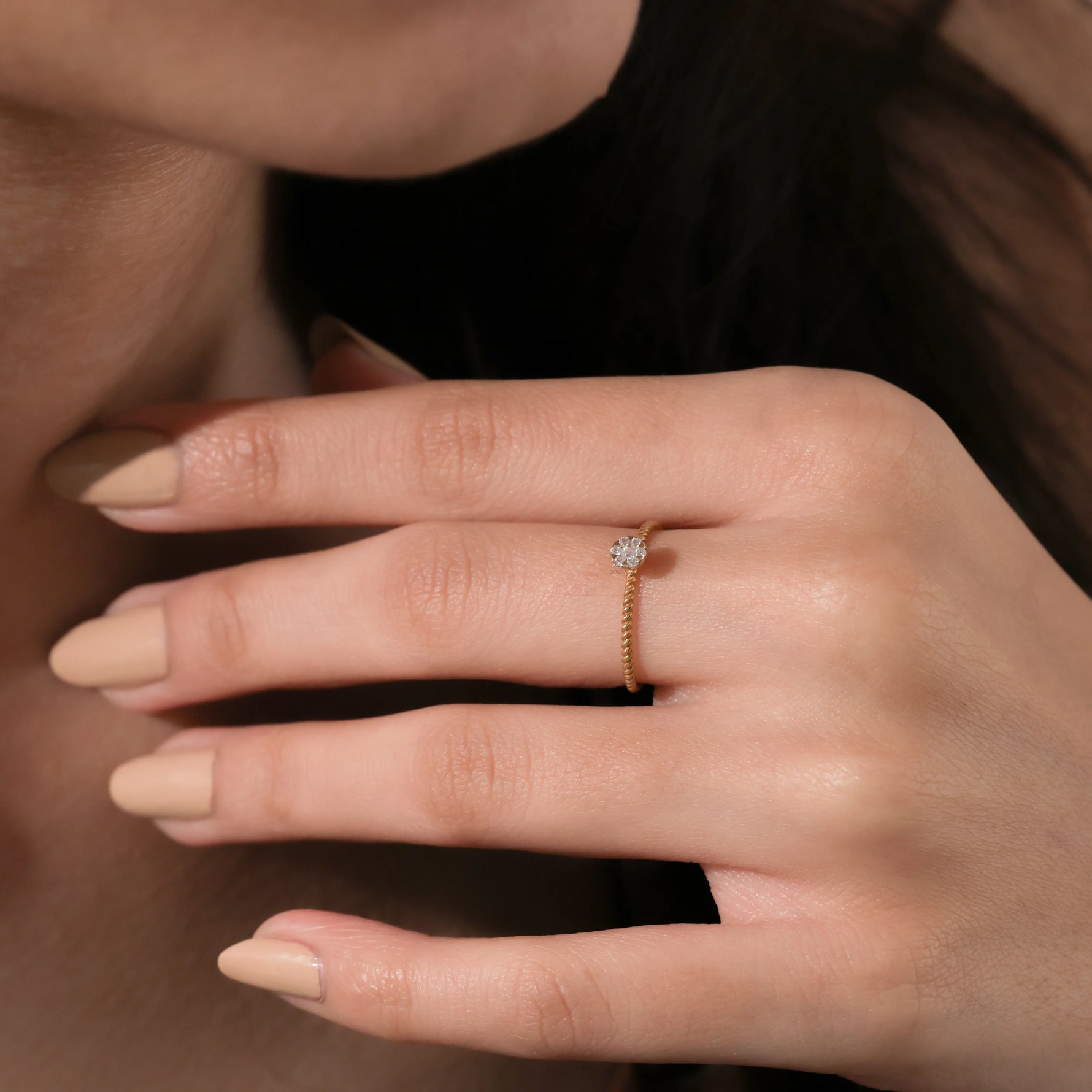 Close up of a delicate 14k yellow gold stackable ring with a small circular diamond cluster setting on a finger with nude manicure.