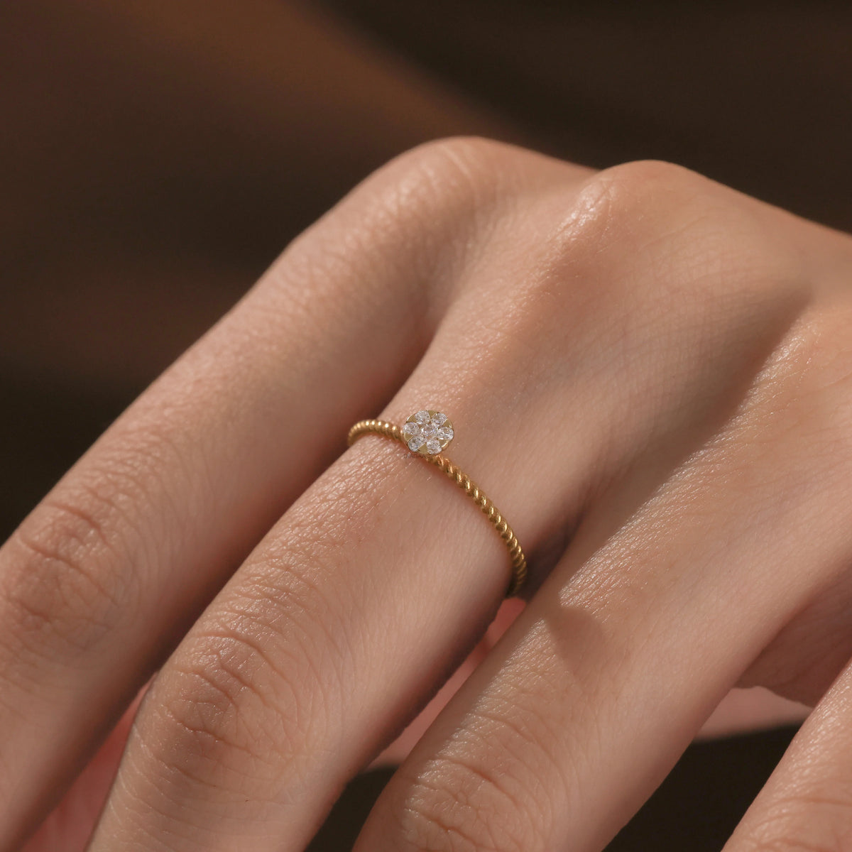 Detailed view of a fine Close-up of a hand wearing a dainty yellow gold twisted band ring featuring a round small diamond cluster centerpiece.