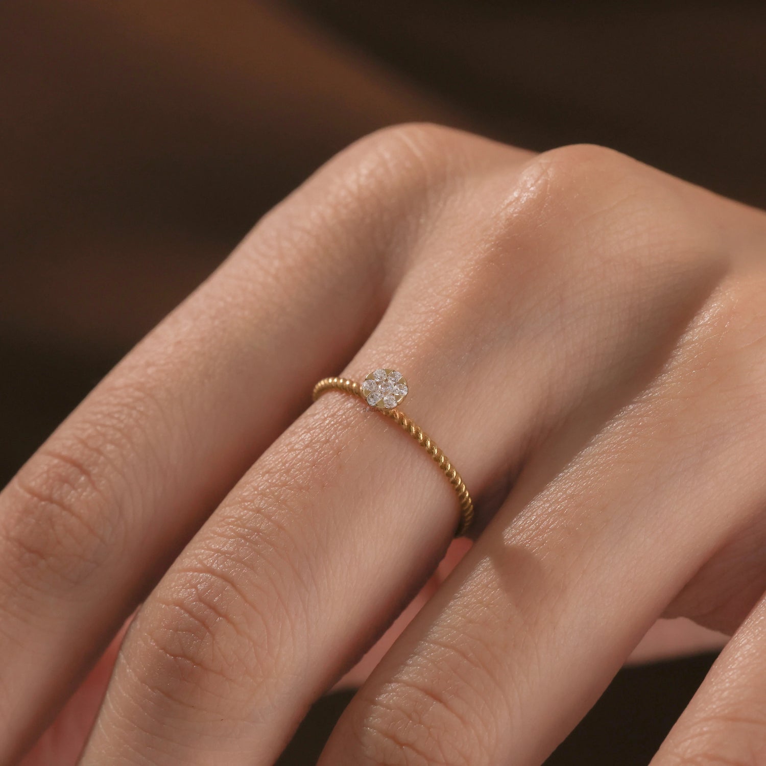 Detailed view of a fine Close-up of a hand wearing a dainty yellow gold twisted band ring featuring a round small diamond cluster centerpiece.