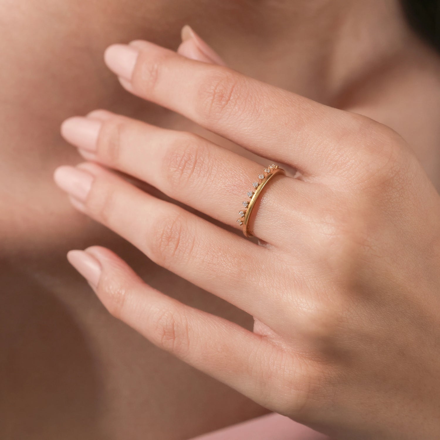 Elegant fine jewelry showcase featuring a thin gold band ring with tiny embedded diamonds worn on a finger.