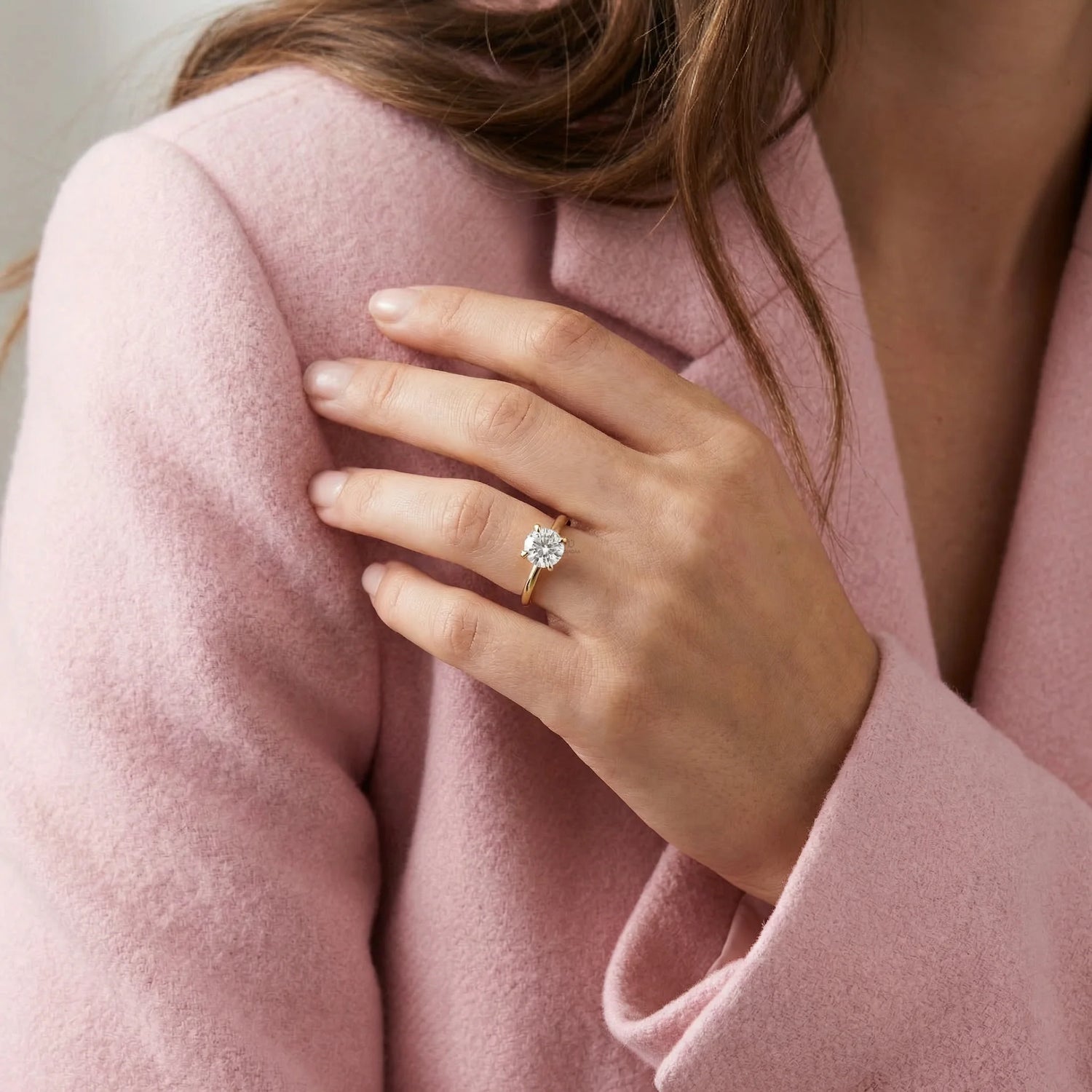 Woman wearing a classic round solitaire diamond engagement ring with a yellow gold band on her hand.