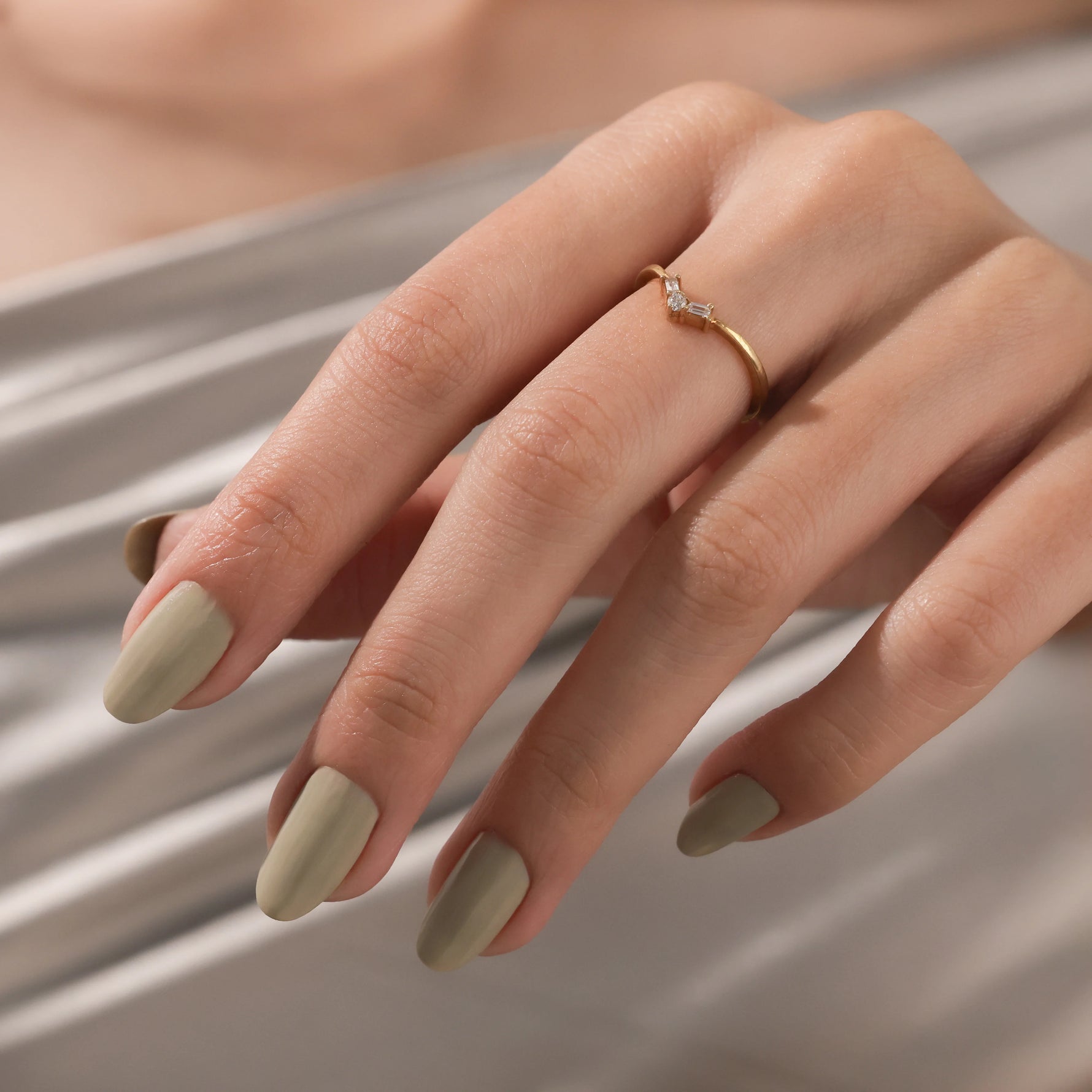 Model wearing a dainty gold chevron ring with baguette diamonds on her finger. Elegant V-shaped curved wedding band.