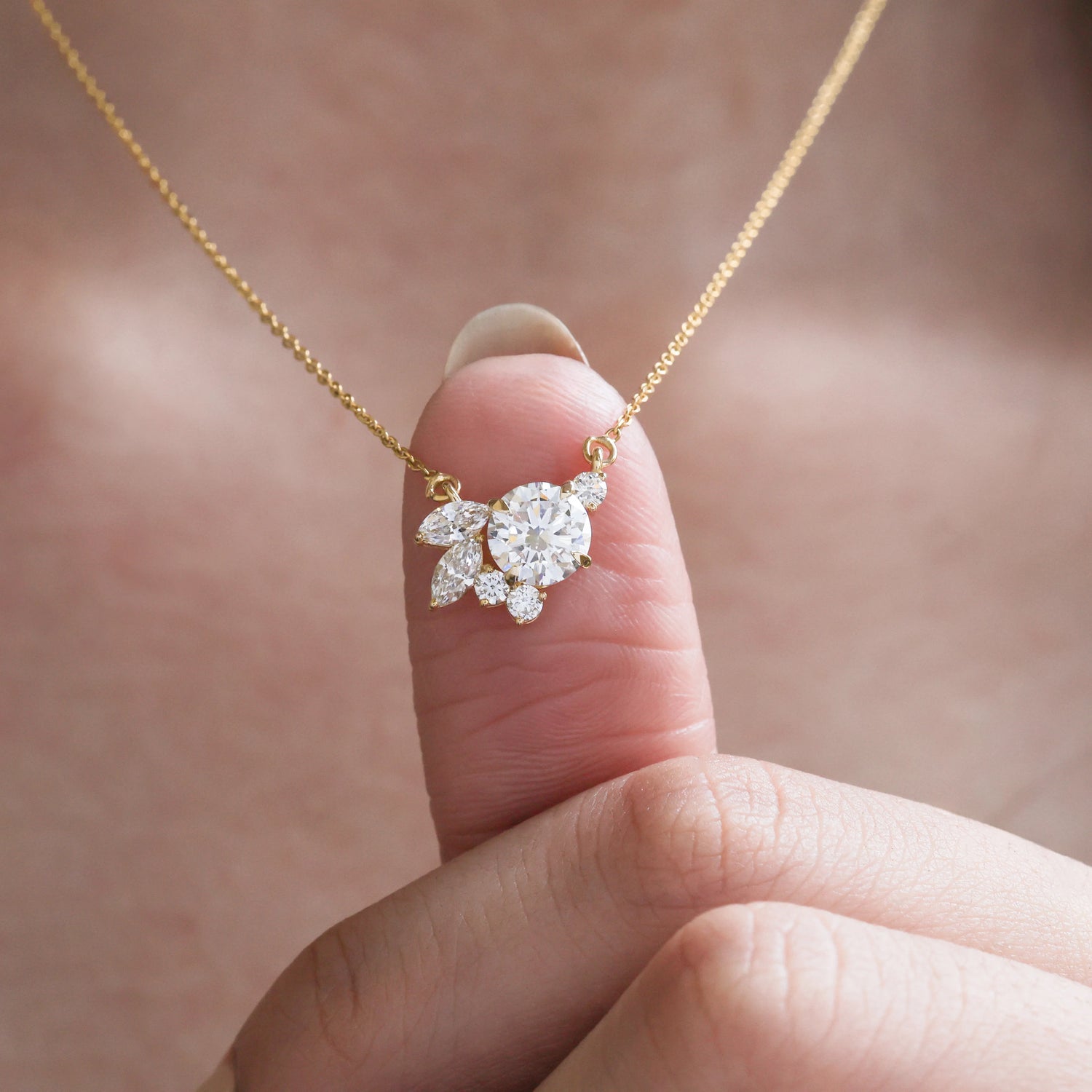 Gold necklace with a diamond pendant held by a hand against a blurred background