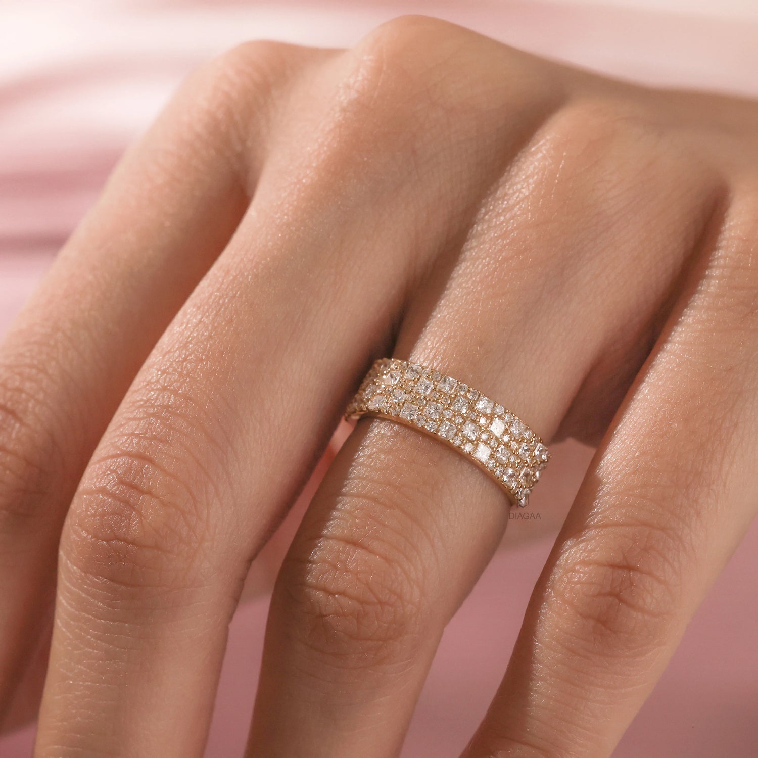 Elegant multi-row pave set princess and round diamond wedding band in yellow gold , worn on a finger. A beautiful statement jewelry piece shown close up.