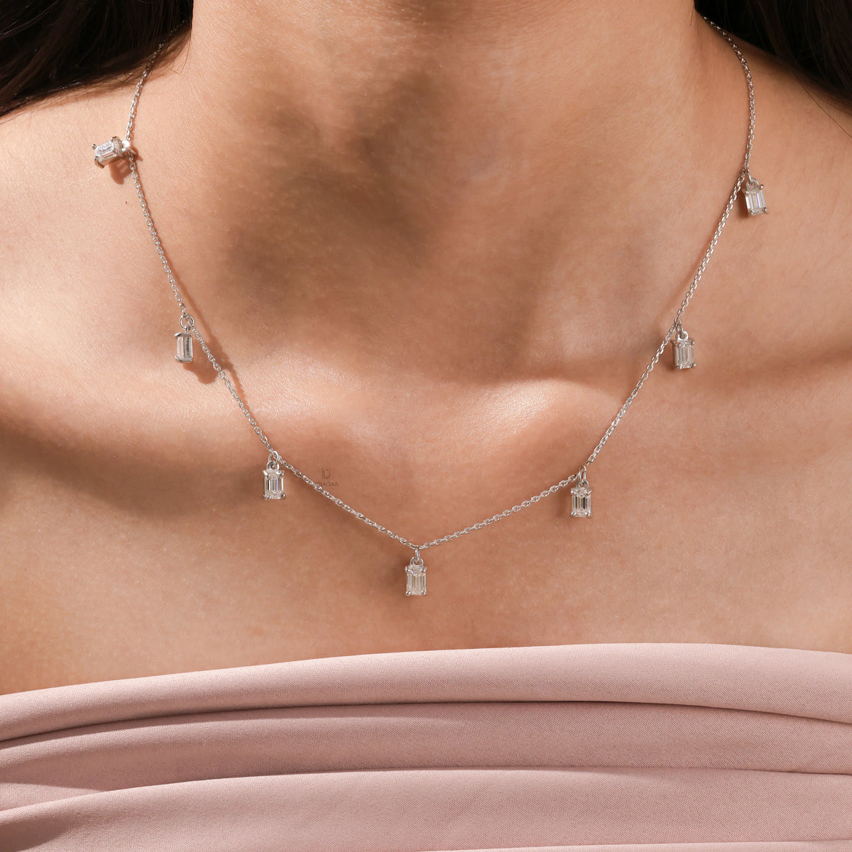 Model wearing an Emerald diamond Dangling necklace, also available in yellow gold with a white background, featuring seven prong-set stones.