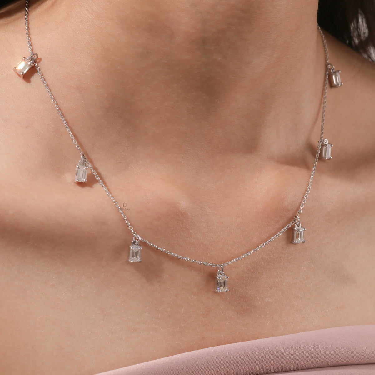 Model wearing an Emerald diamond Dangling necklace, also available in yellow gold with a white background, featuring seven prong-set stones.