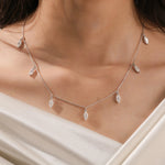 Elegant seven-stone prong-set marquise diamond dangling necklace in yellow gold, styled gracefully on a model's neckline above white silk.