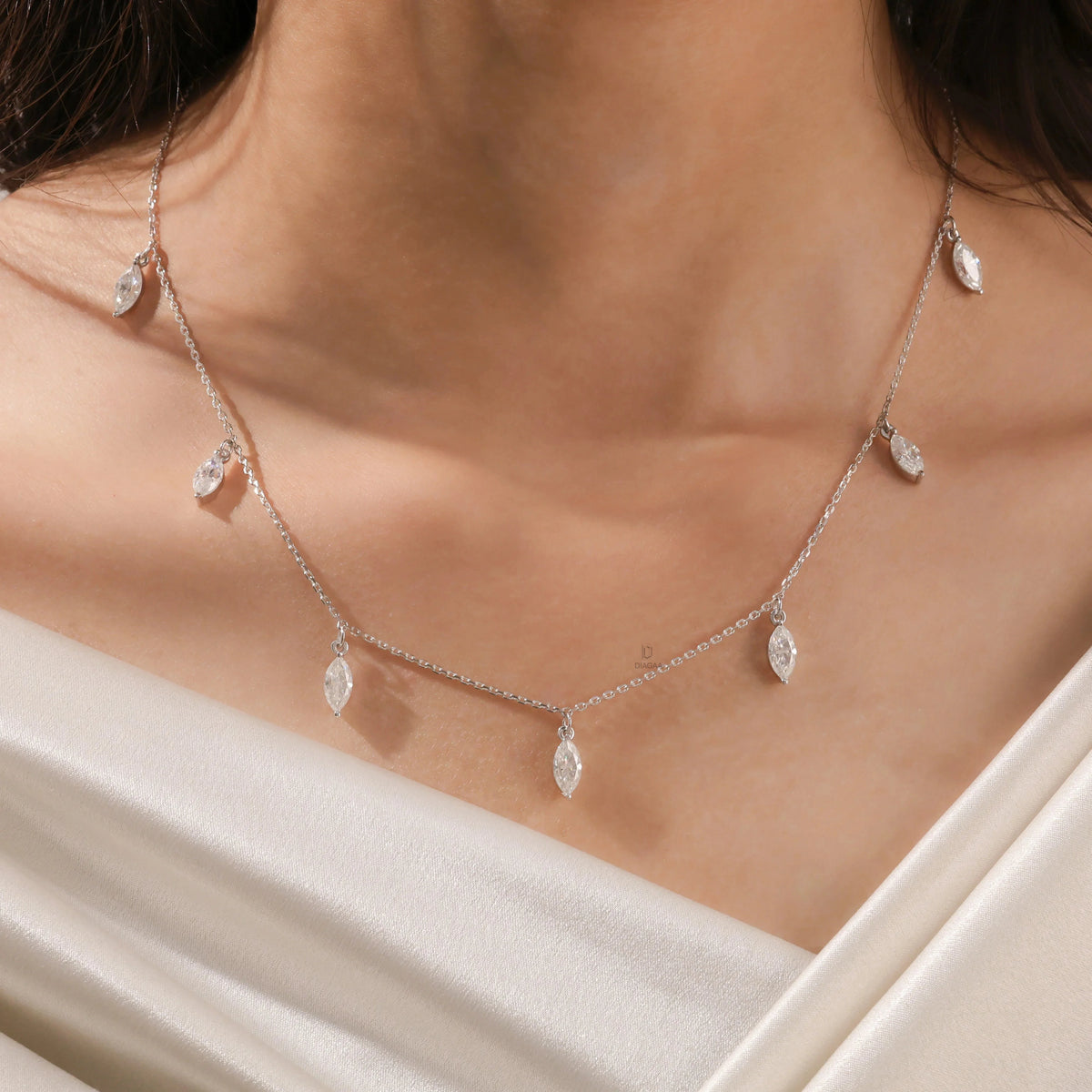 Elegant seven-stone prong-set marquise diamond dangling necklace in yellow gold, styled gracefully on a model's neckline above white silk.