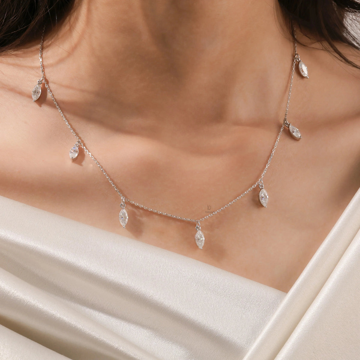 Elegant seven-stone prong-set marquise diamond dangling necklace in yellow gold, styled gracefully on a model's neckline above white silk.