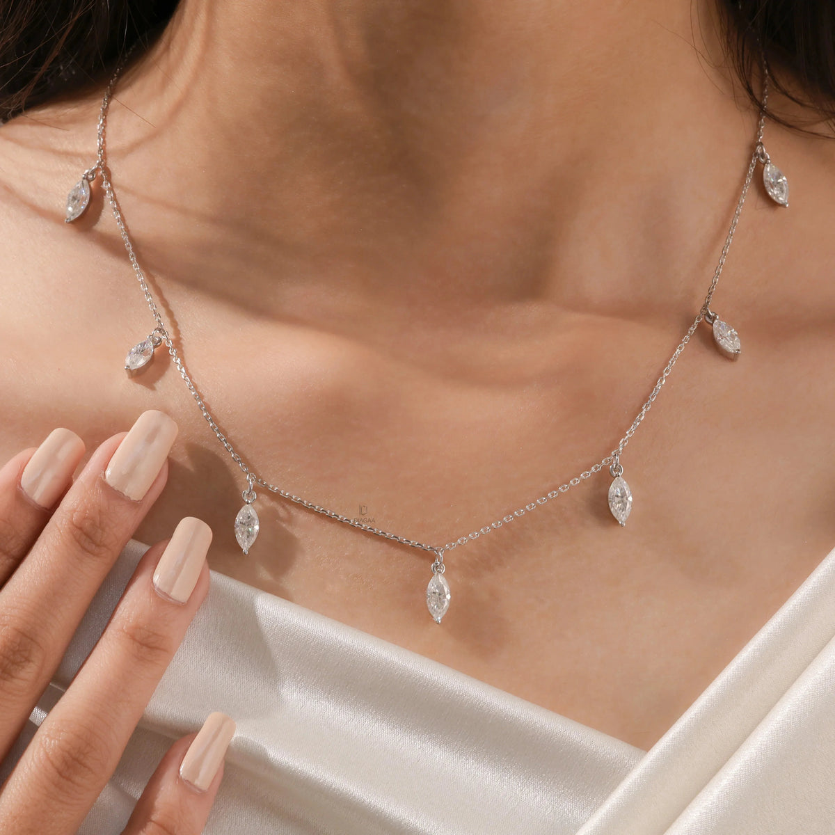Elegant seven-stone prong-set marquise diamond dangling necklace in yellow gold, styled gracefully on a model's neckline above white silk.