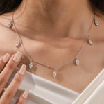 Elegant seven-stone prong-set marquise diamond dangling necklace in yellow gold, styled gracefully on a model's neckline above white silk.