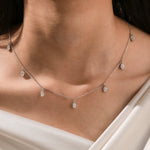Close-up of a model's neckline highlighting a dainty yellow gold chain and a stunning prong-set Oval diamond dangling necklace with seven drop stones.