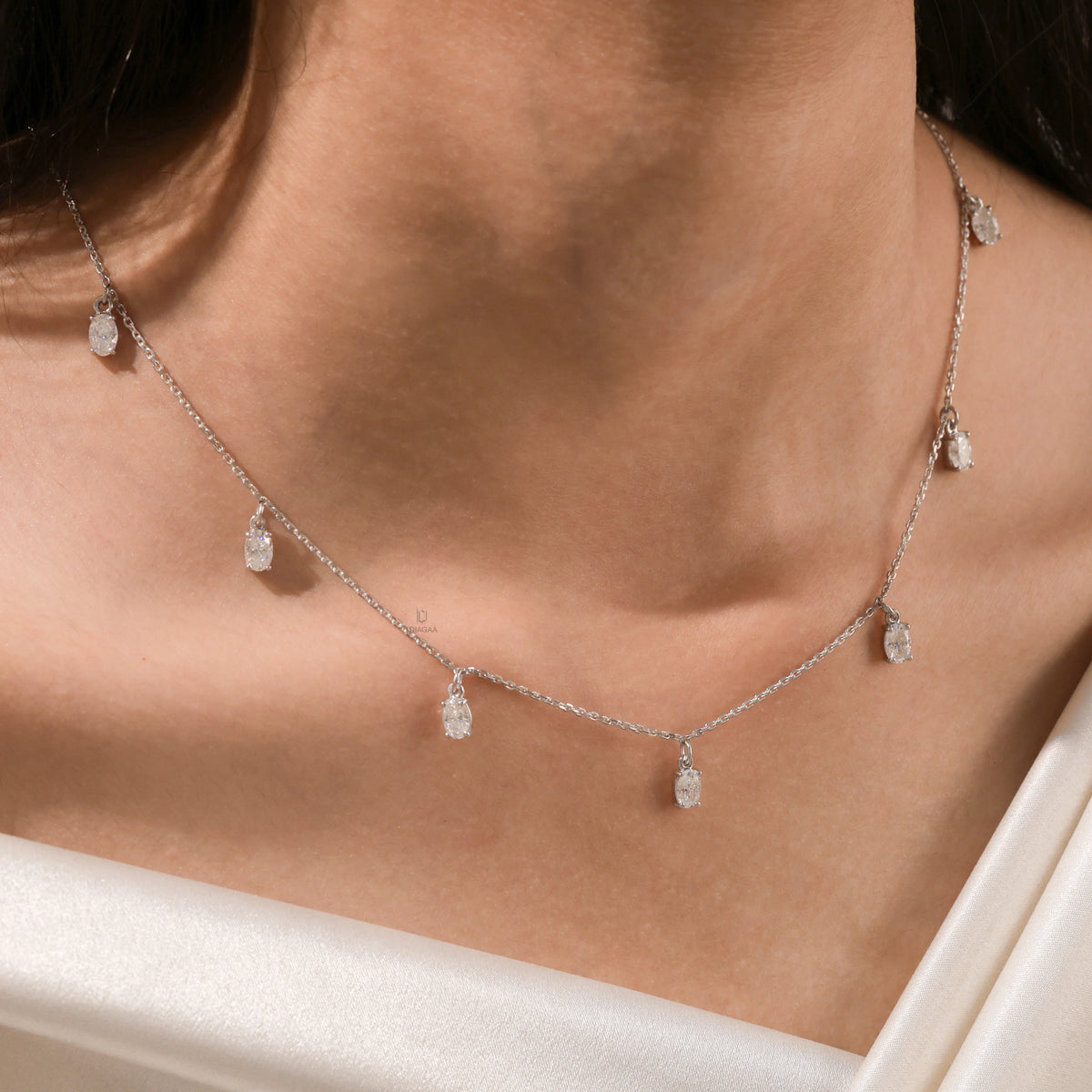 Close-up of a model's neckline highlighting a dainty yellow gold chain and a stunning prong-set Oval diamond dangling necklace with seven drop stones.