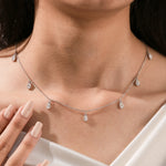 Close-up of a model's neckline highlighting a dainty yellow gold chain and a stunning prong-set Oval diamond dangling necklace with seven drop stones.