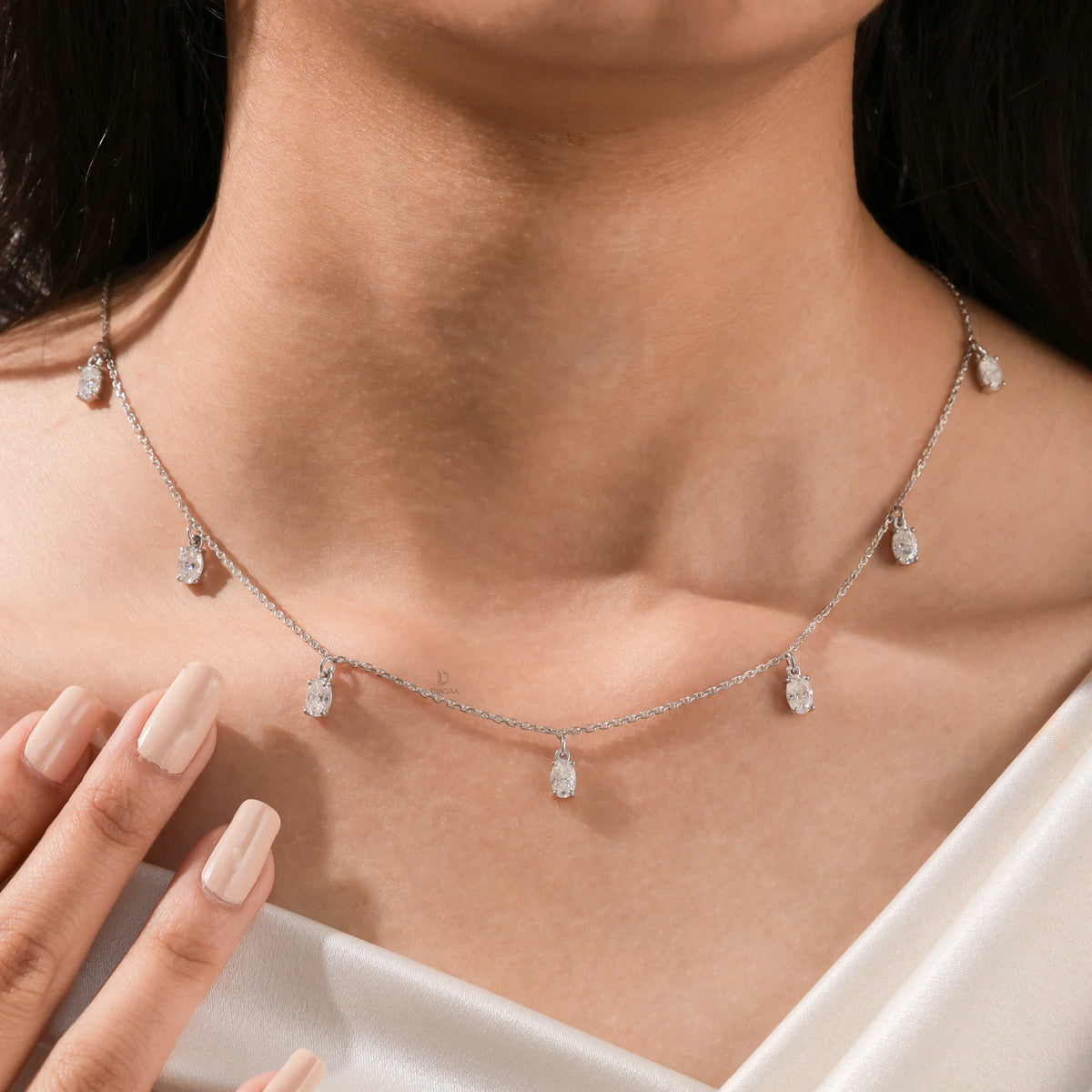 Close-up of a model's neckline highlighting a dainty yellow gold chain and a stunning prong-set Oval diamond dangling necklace with seven drop stones.