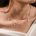 Close-up of a model's neckline highlighting a dainty yellow gold chain and a stunning prong-set Oval diamond dangling necklace with seven drop stones.