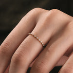 hand wearing a A thin yellow gold stackable diamond band featuring a minimalist beaded design with small brilliant cut accent diamonds being worn on a hand.