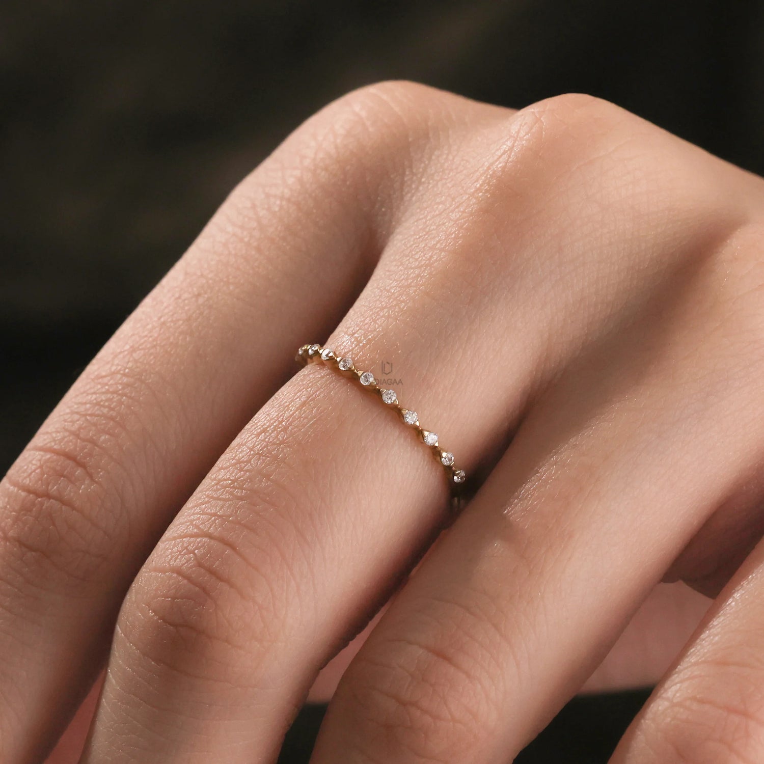 hand wearing a A thin yellow gold stackable diamond band featuring a minimalist beaded design with small brilliant cut accent diamonds being worn on a hand.