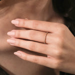 Close up of a dainty yellow gold diamond wedding band or promise ring showing a delicate geometric setting on a finger.