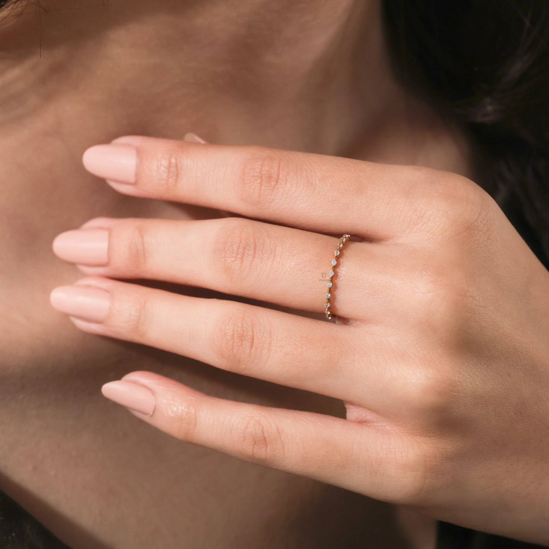 Close up of a dainty yellow gold diamond wedding band or promise ring showing a delicate geometric setting on a finger.