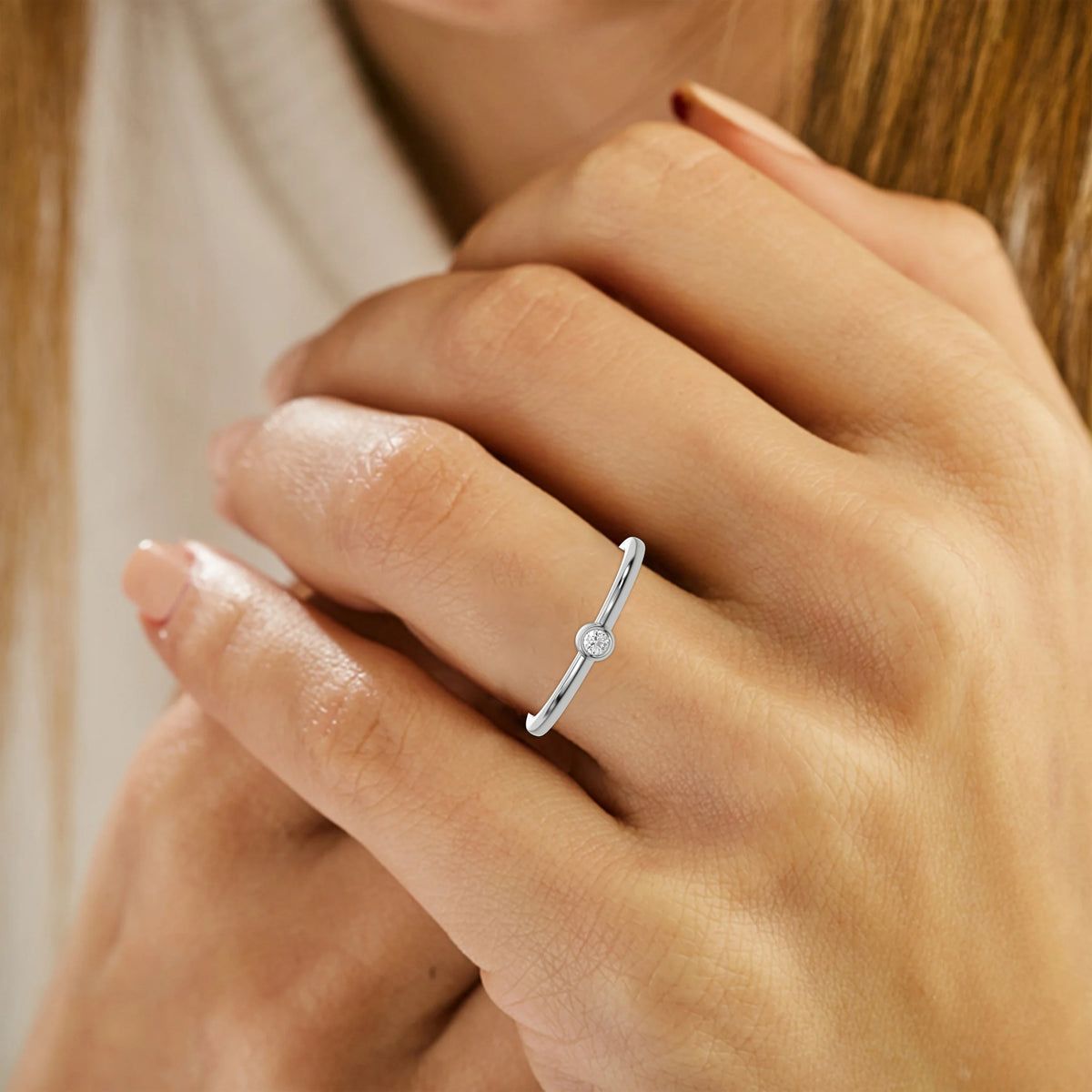 Thin white gold band with a round solitaire diamond in bezel setting on ring finger