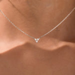 Woman wearing a delicate three-stone round diamond necklace featuring a prong-set cluster in 18K white gold.