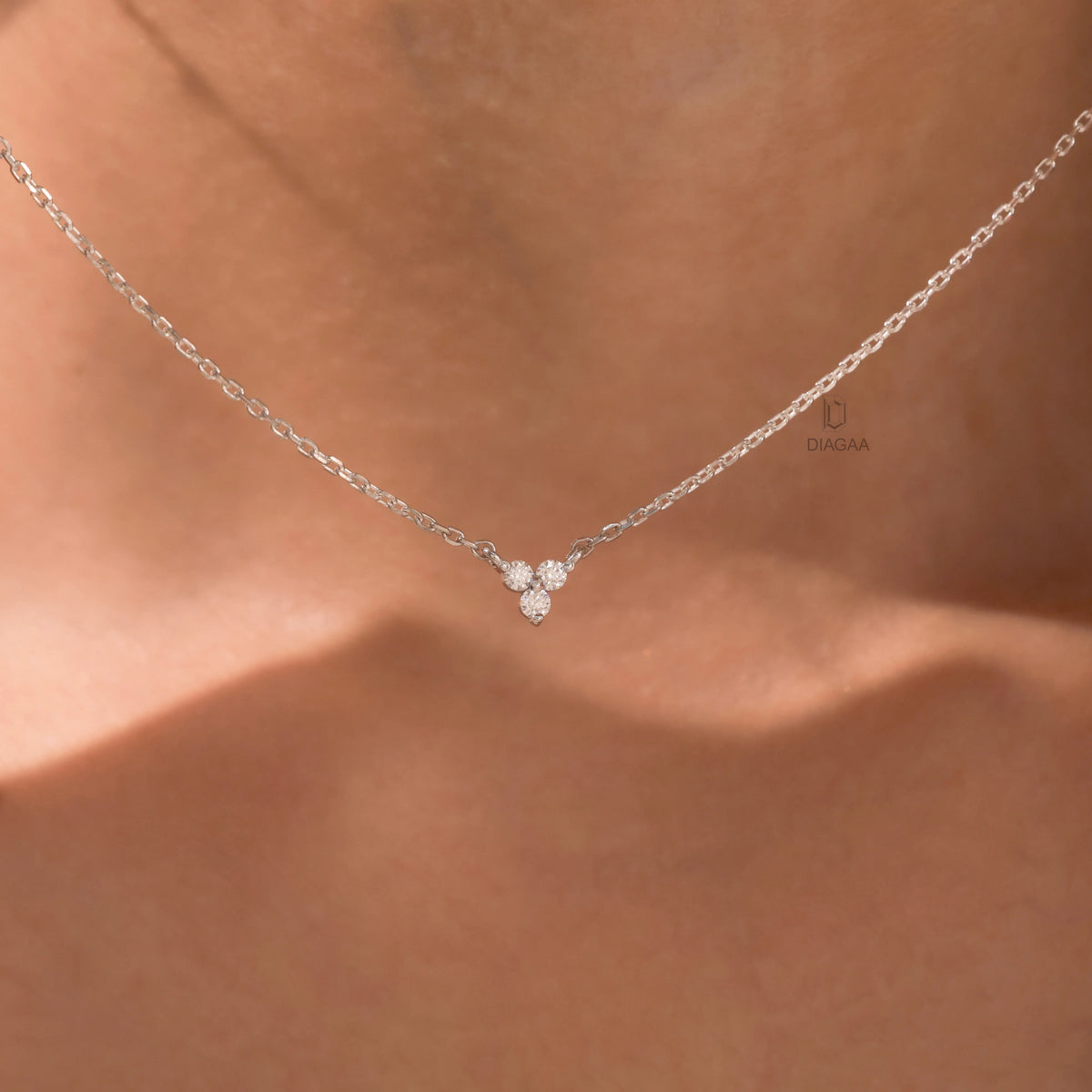 Woman wearing a delicate three-stone round diamond necklace featuring a prong-set cluster in 18K white gold.