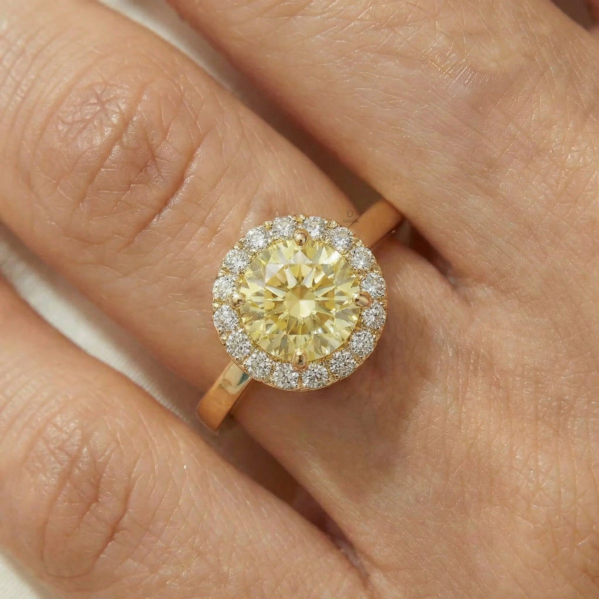 Elegant round yellow diamond halo engagement ring in yellow gold,modeled gracefully on a woman's hand.