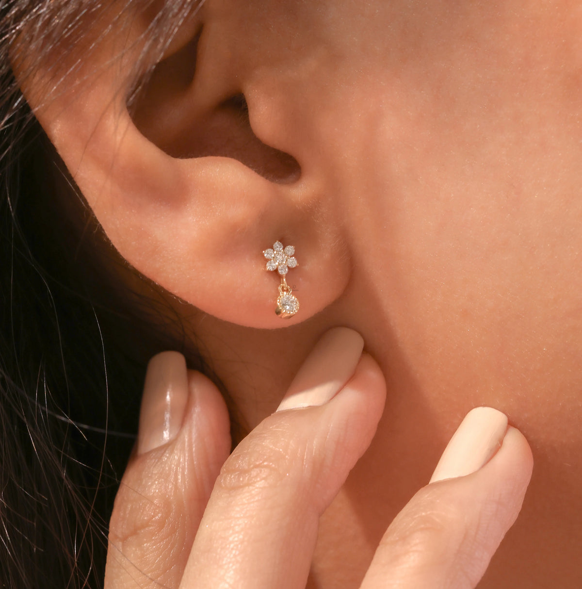 Close-up of a woman wearing a delicate yellow gold diamond drop earring featuring a tiny floral cluster and dangling round diamond.