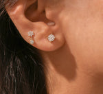 Close-up of a curated ear featuring a 14k yellow gold round diamond stud in the main lobe and a dainty floral diamond drop earring in the second piercing.