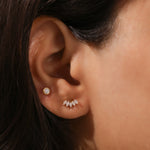 Woman's ear with a yellow gold marquise diamond fan stud in the main piercing and a bezel-set round diamond stud in the upper lobe