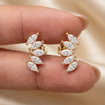 Hand holding a pair of yellow gold marquise diamond climber earrings arranged in a curved leaf cluster design.