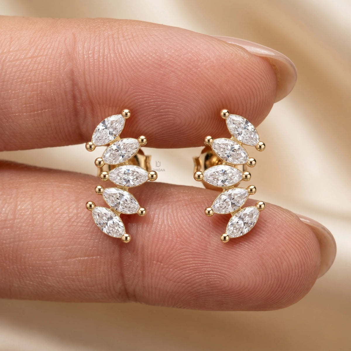 Hand holding a pair of yellow gold marquise diamond climber earrings arranged in a curved leaf cluster design.