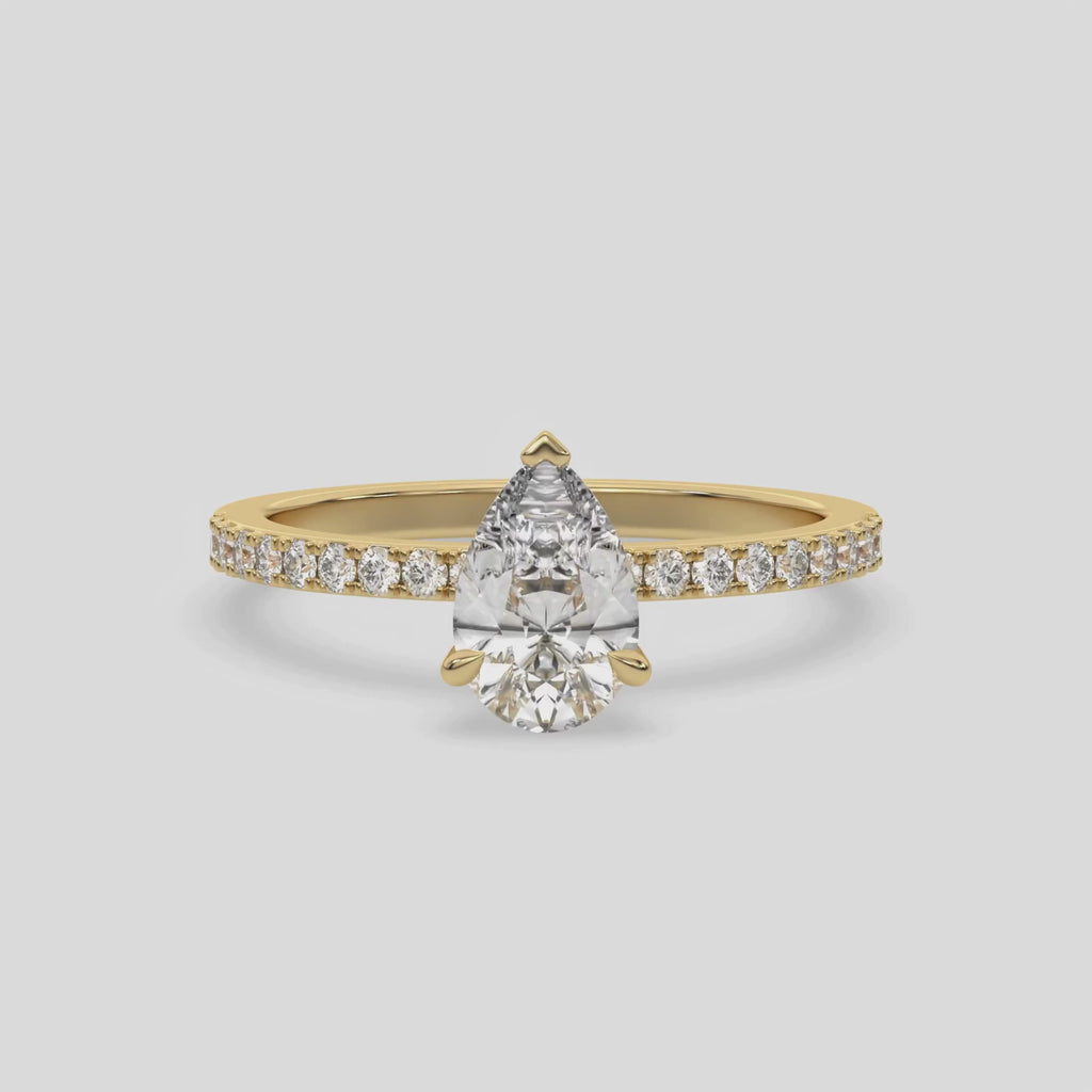 This video features a yellow gold ring is made with a pear solitaire diamond set in three-prong setting, and is complemented by a round pave diamonds band