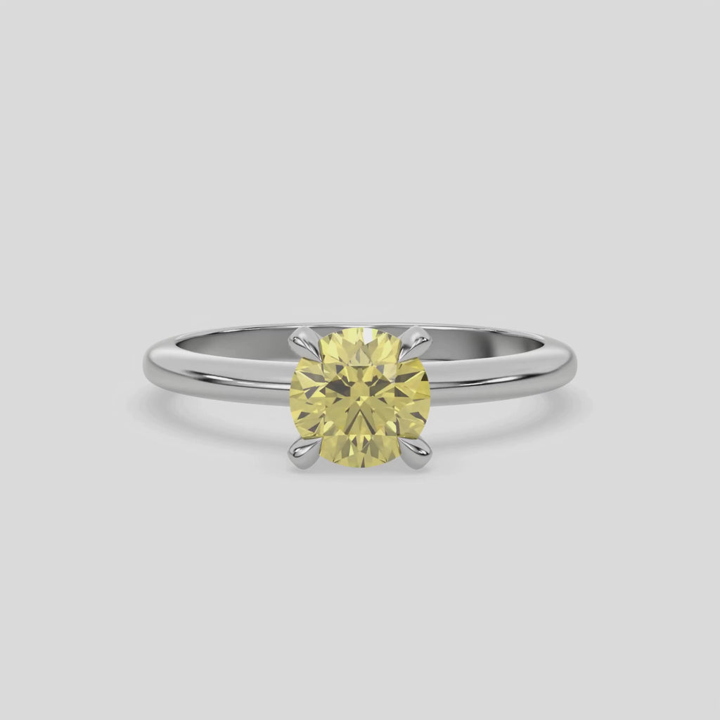 This video features a white gold ring features a fancy Yellow round solitaire diamond elegantly secured in a four-prong setting on a solid gold band