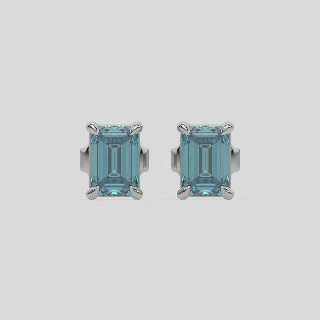 This video features a white gold Classic Emerald Diamond Earrings made with an fancy blue emerald-cut diamonds set in a four prong setting