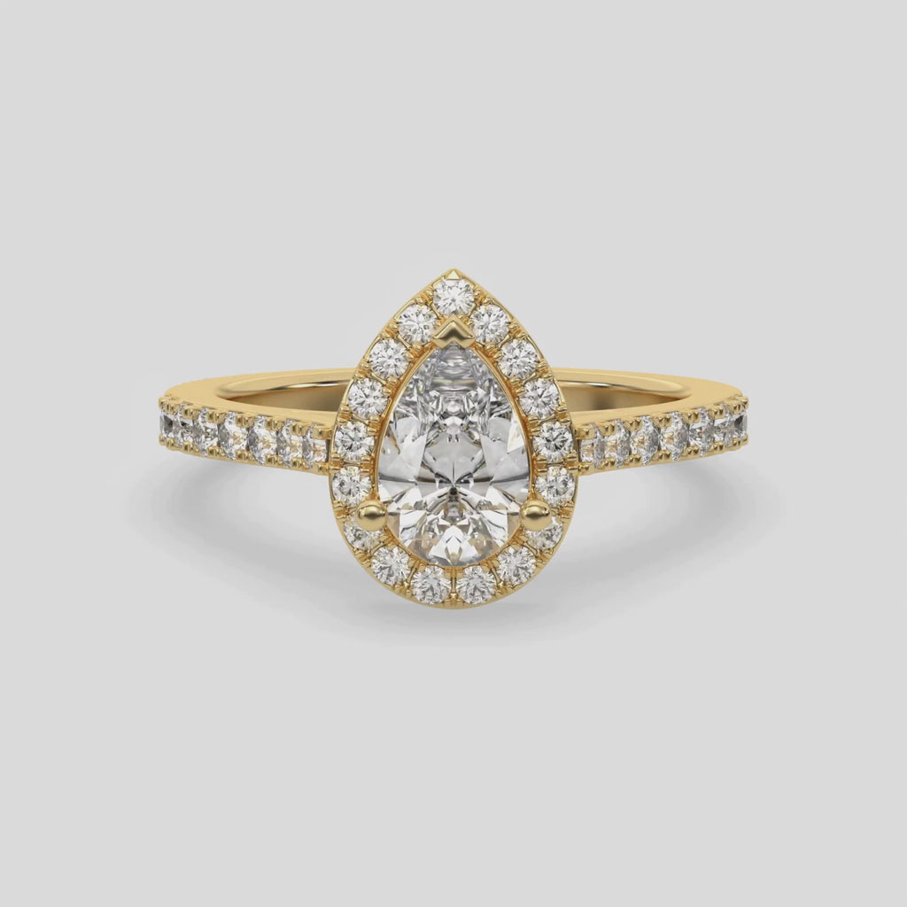 This video features a yellow gold Pear Diamond Halo Engagement Ring is made with a pear solitaire diamond set in a four-prong setting, surrounded by a halo of round diamonds all set on a pave band 