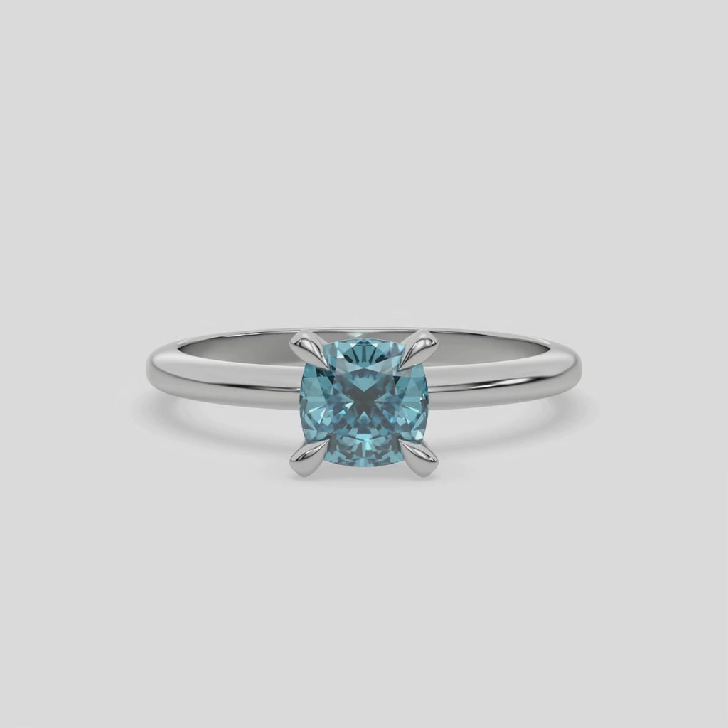 This video features a white gold ring features a fancy Blue cushion solitaire diamond elegantly secured in a four-prong setting on a solid gold band