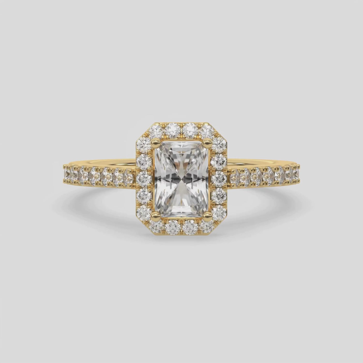 This video features a yellow gold Radiant Diamond Halo Engagement Ring is made with a radiant solitaire diamond set in a four-prong setting, surrounded by a halo of round diamonds all set on a pave band