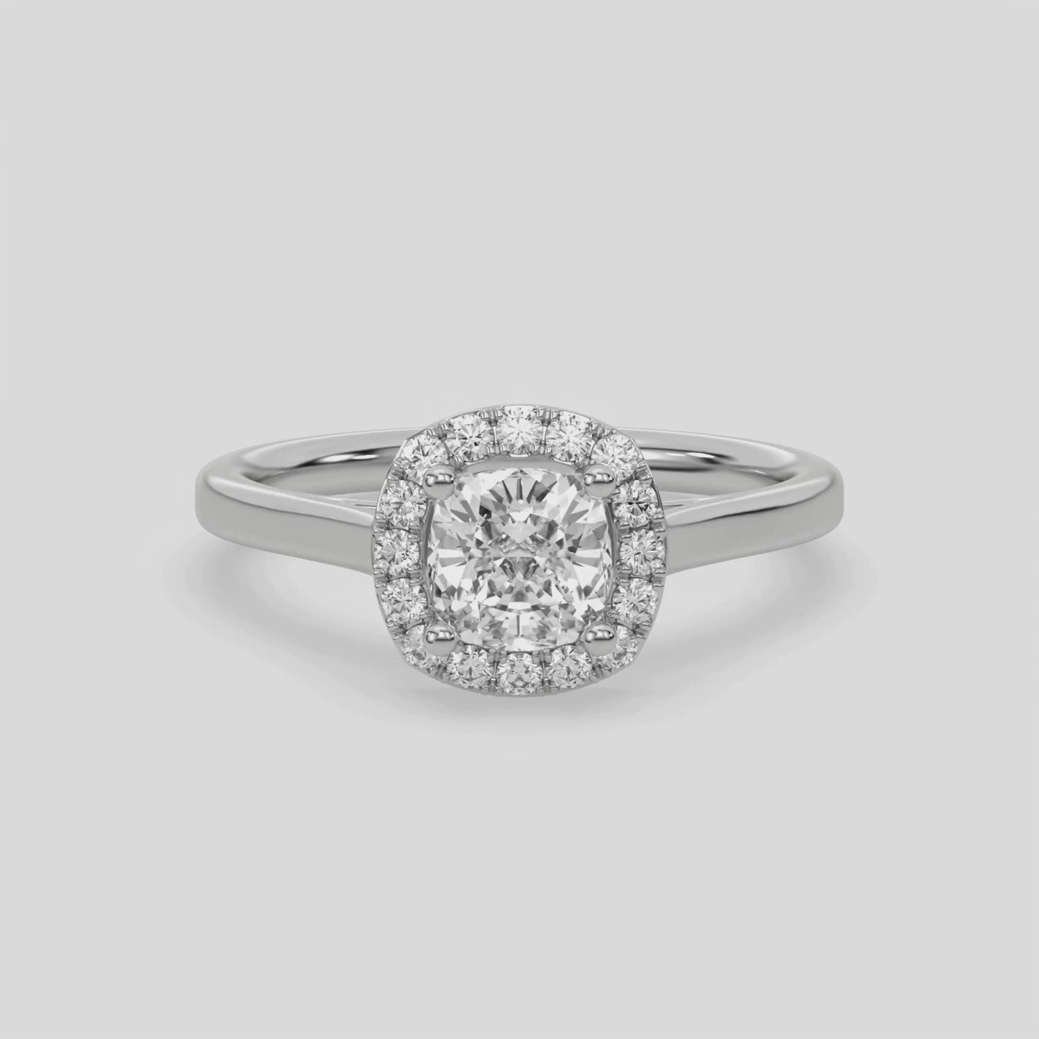 This video features a white gold ring features a cushion solitaire diamond set in a four-prong setting, surrounded by a halo of round diamonds, all resting on a delicate gold band