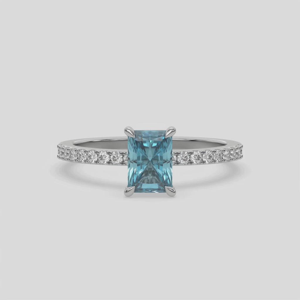 This video features a white gold ring is made with a fancy Blue radiant solitaire diamond set in four-prong setting, and is complemented by a round pave diamonds band