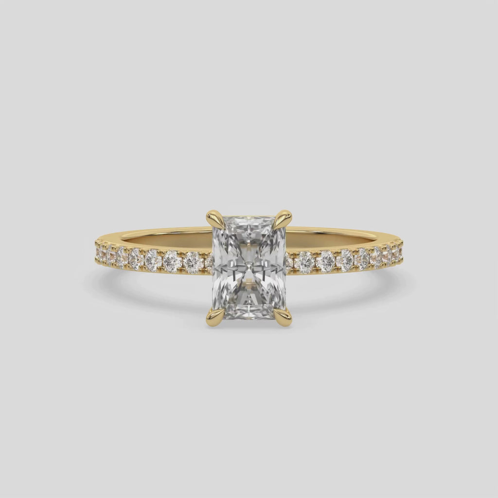 This video features a yellow gold  ring is made with a radiant solitaire diamond set in four-prong setting, and is complemented by a round pave diamonds band