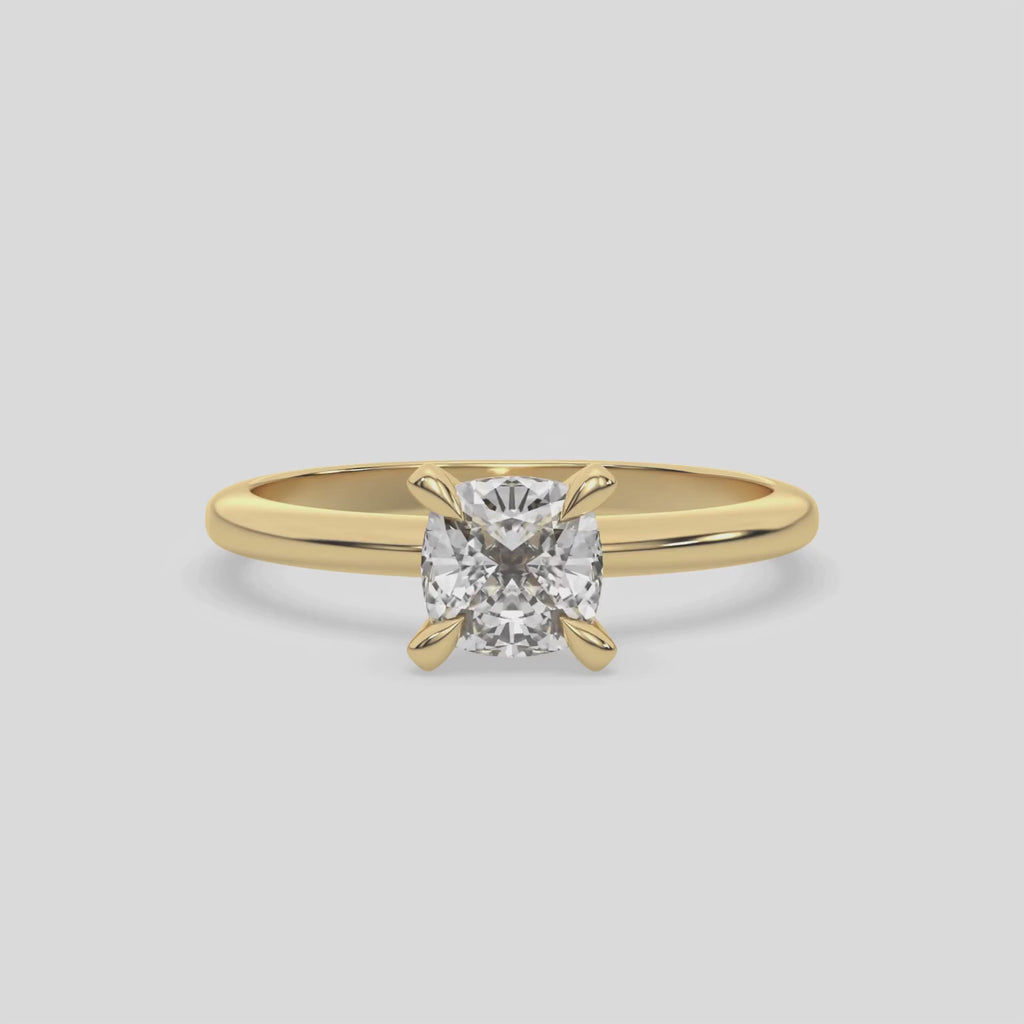 This video features a yellow gold ring features a cushion solitaire diamond elegantly secured in a four-prong setting on a solid gold band 