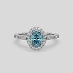 This video features a white gold Oval Diamond Halo Engagement Ring is made with a fancy blue oval solitaire diamond set in a four-prong setting, surrounded by a halo of round diamonds all set on a pave band 