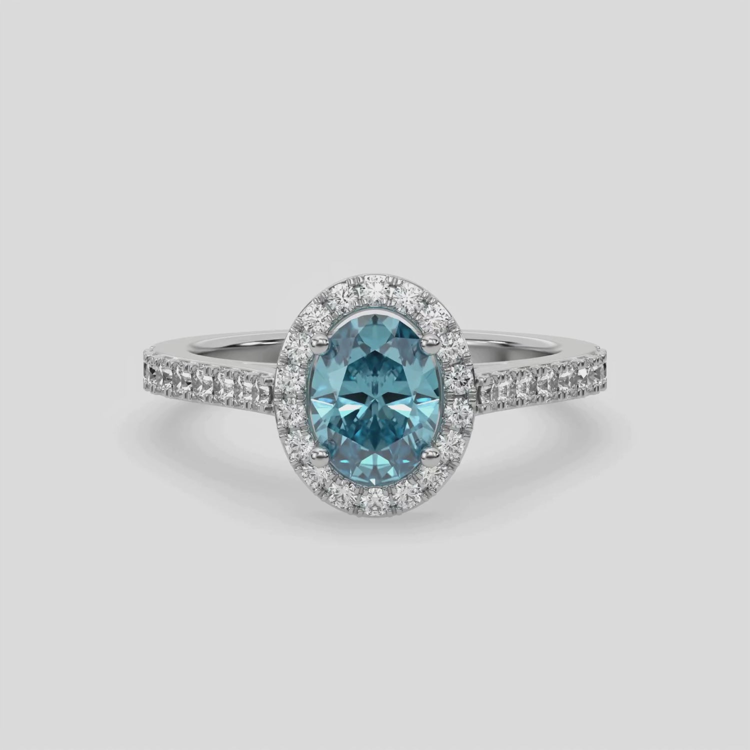 This video features a white gold Oval Diamond Halo Engagement Ring is made with a fancy blue oval solitaire diamond set in a four-prong setting, surrounded by a halo of round diamonds all set on a pave band 